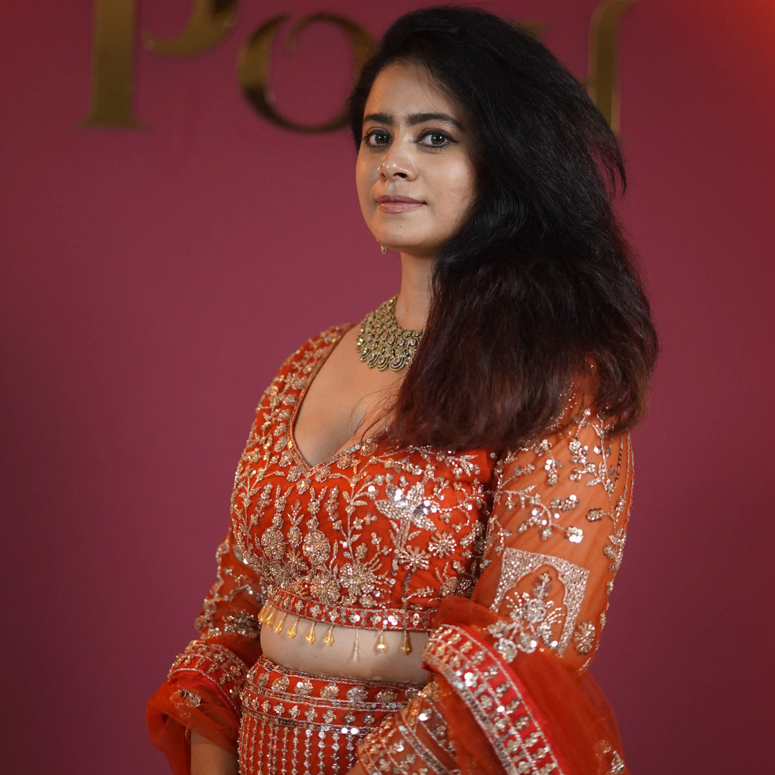 Bride wearing a red embroidered bridal lehenga with traditional jewellery posing in a studio setup at Posh Wedding Rental.