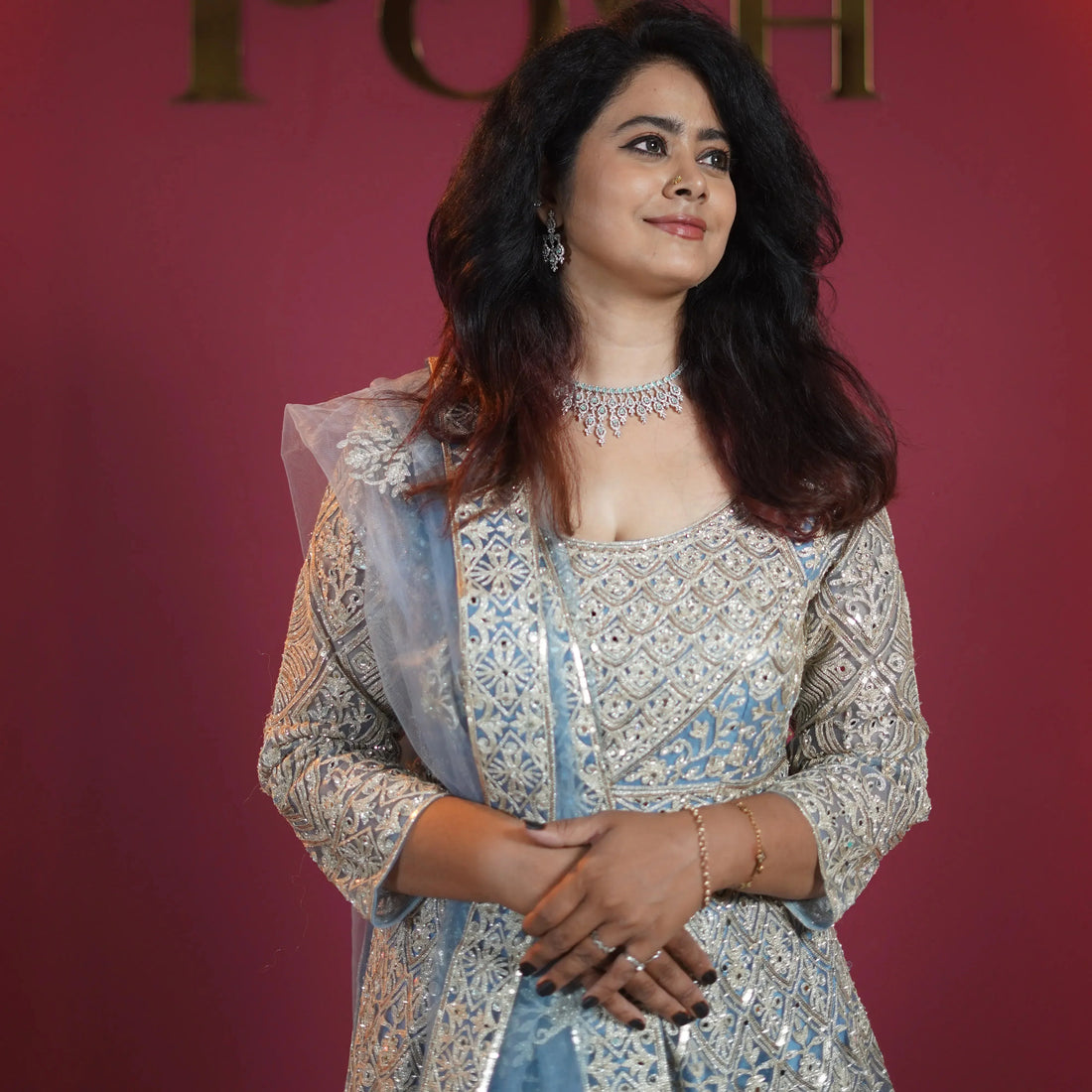 Woman wearing a light blue and gold embroidered bridal lehenga with jewelry, posing against a pink background.