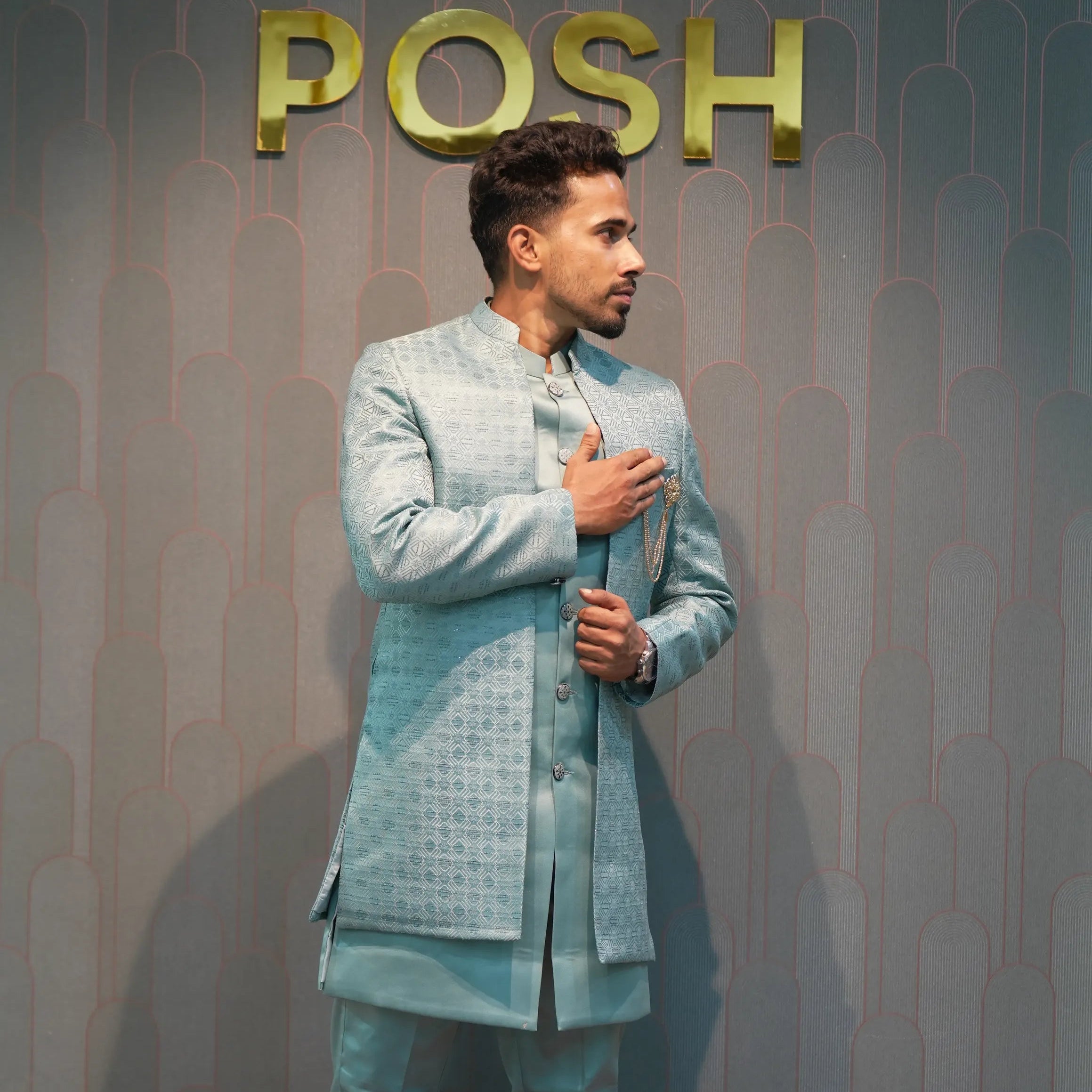 Man in a light blue suit standing in front of a 'POSH' branded wall.
