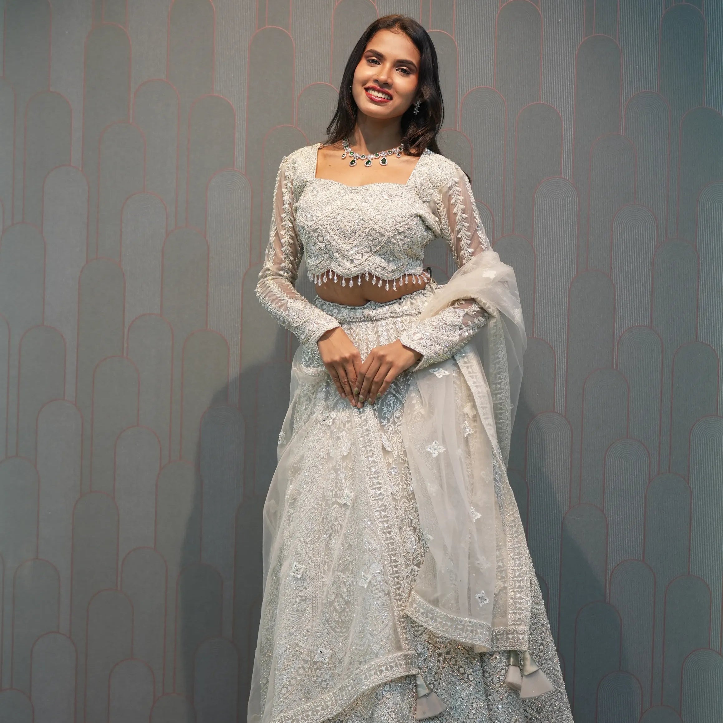 Woman in a white embroidered dress standing in front of a 'POSH' branded wall.