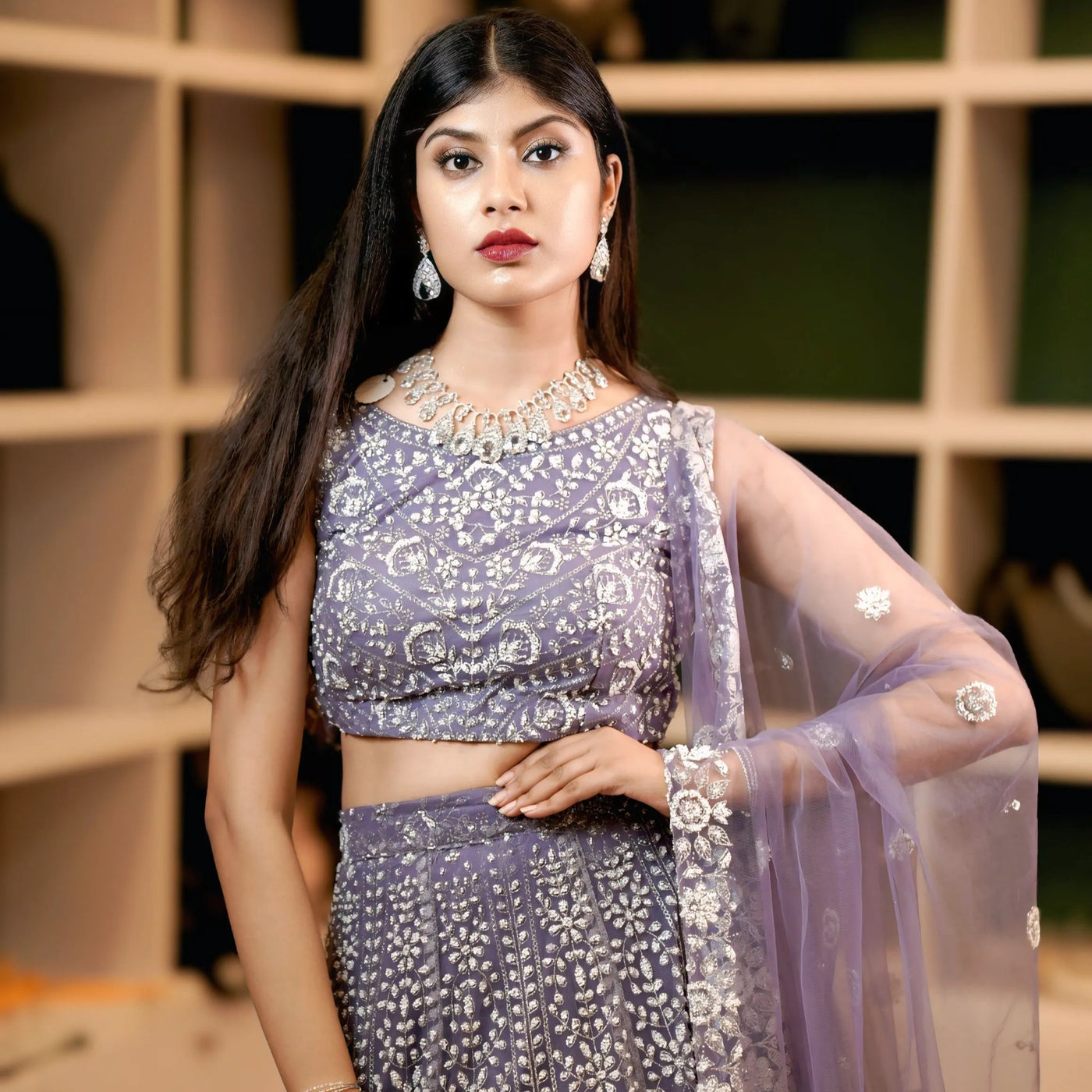 Woman in a purple traditional outfit with silver details against a blurred indoor background