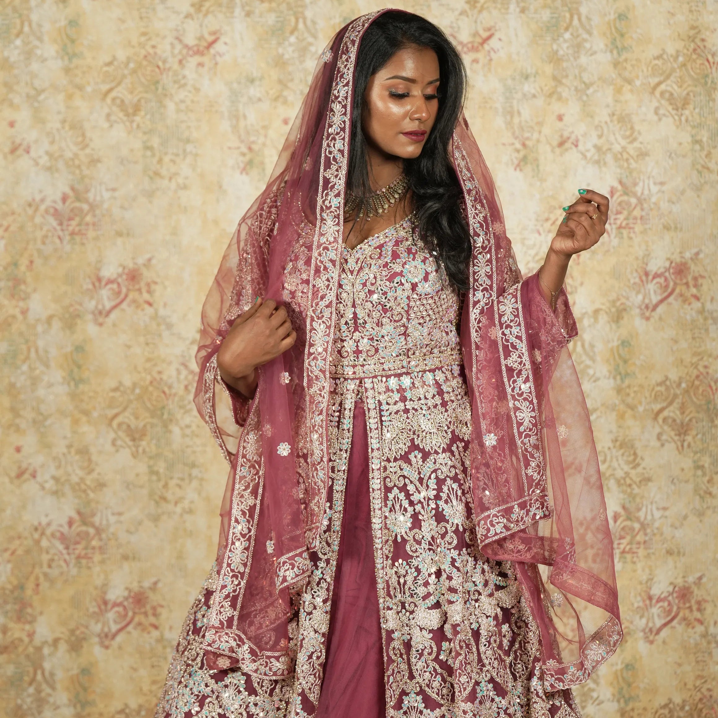 Woman in a traditional outfit with floral patterns against a decorative wall.
